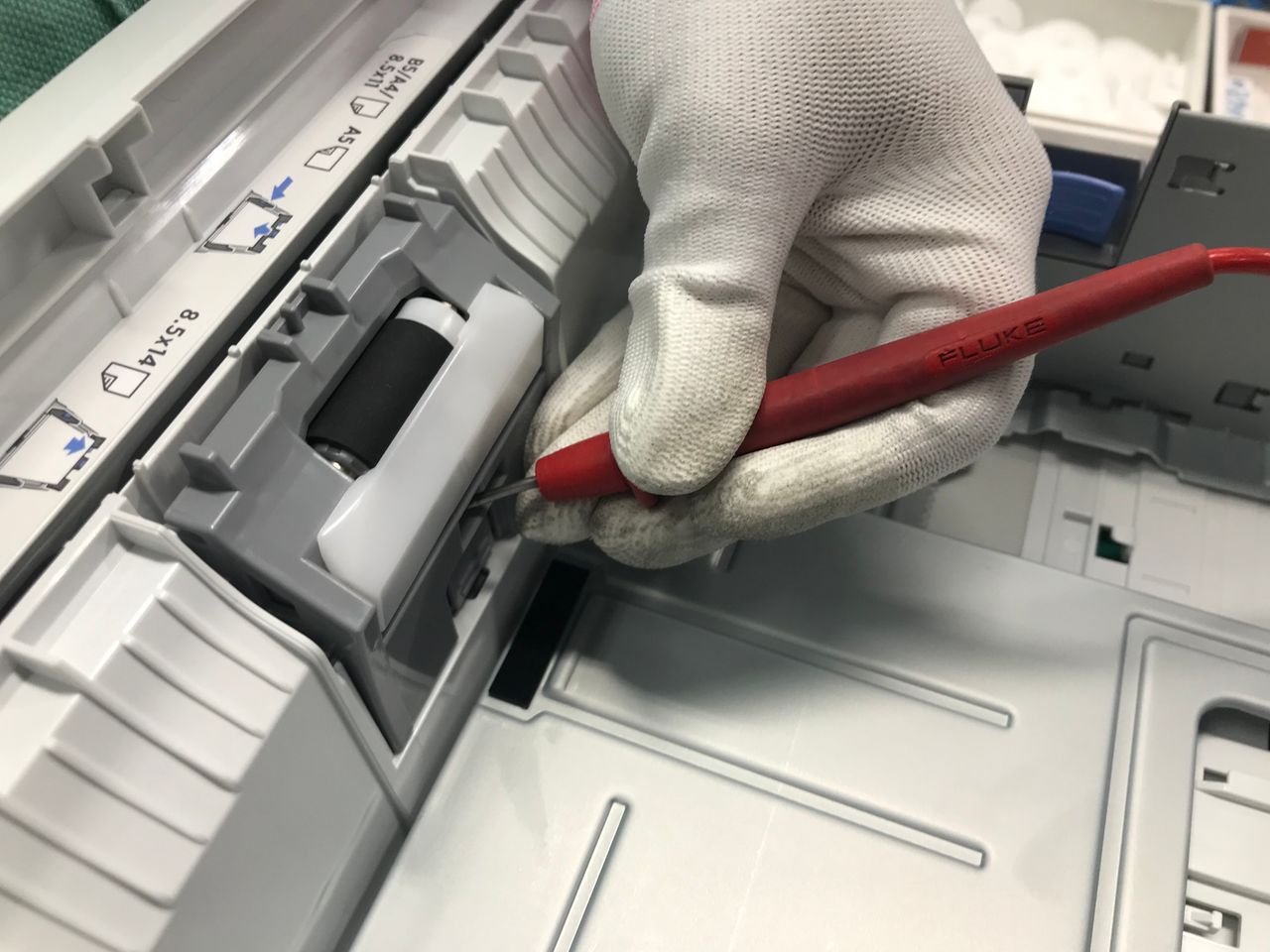 About A gloved hand fixes a printer using a red precision tool, showcasing maintenance skills.