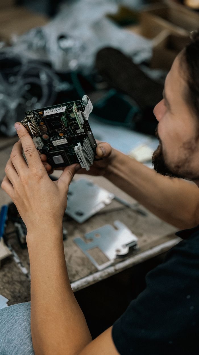 Services Focused technician examining a circuit board with precision in a cluttered workshop environment.